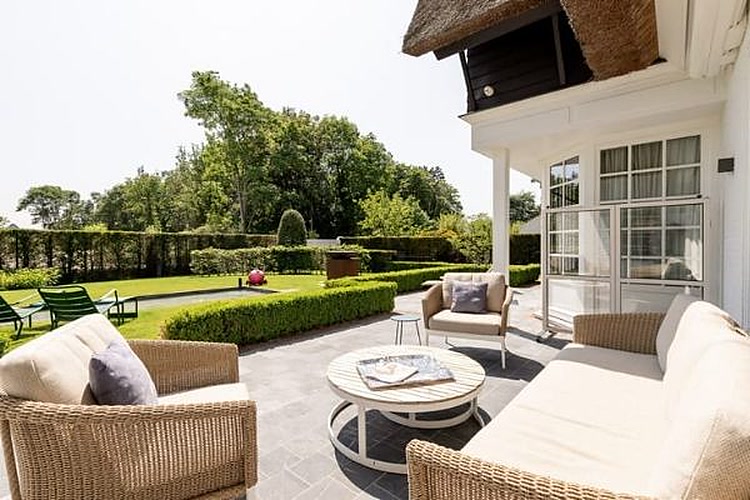 Overdekt terras met loungezetels en uitzicht over het uitgestrekte gazon
